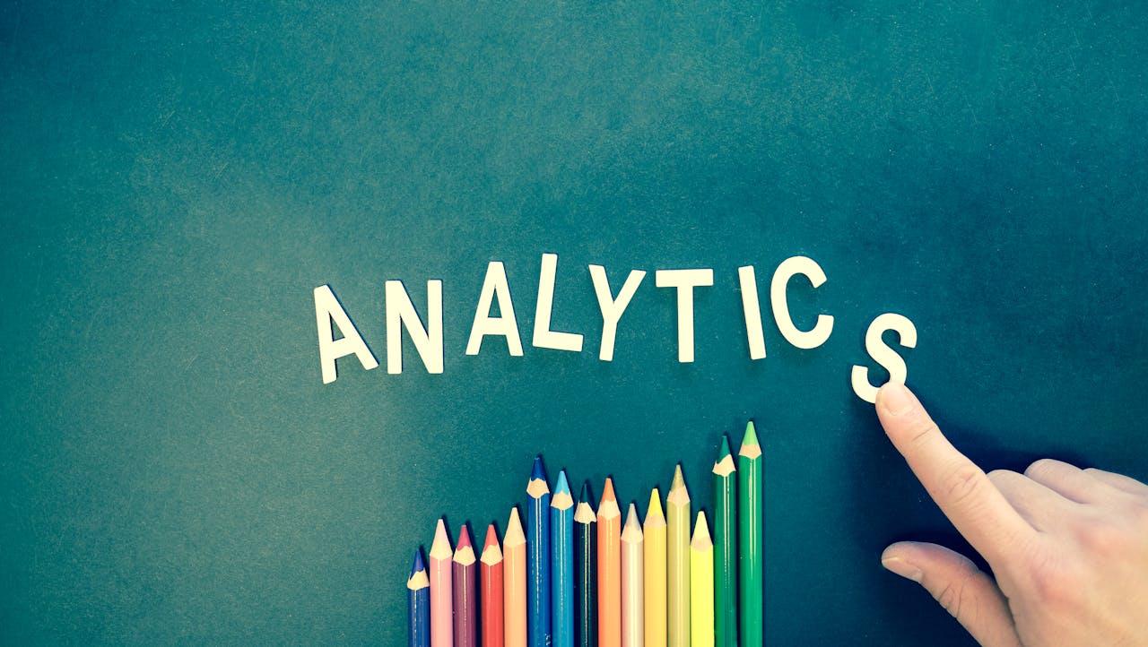 mobile-02 Colored pencils and letters spelling 'ANALYTICS' on a textured background with a hand.