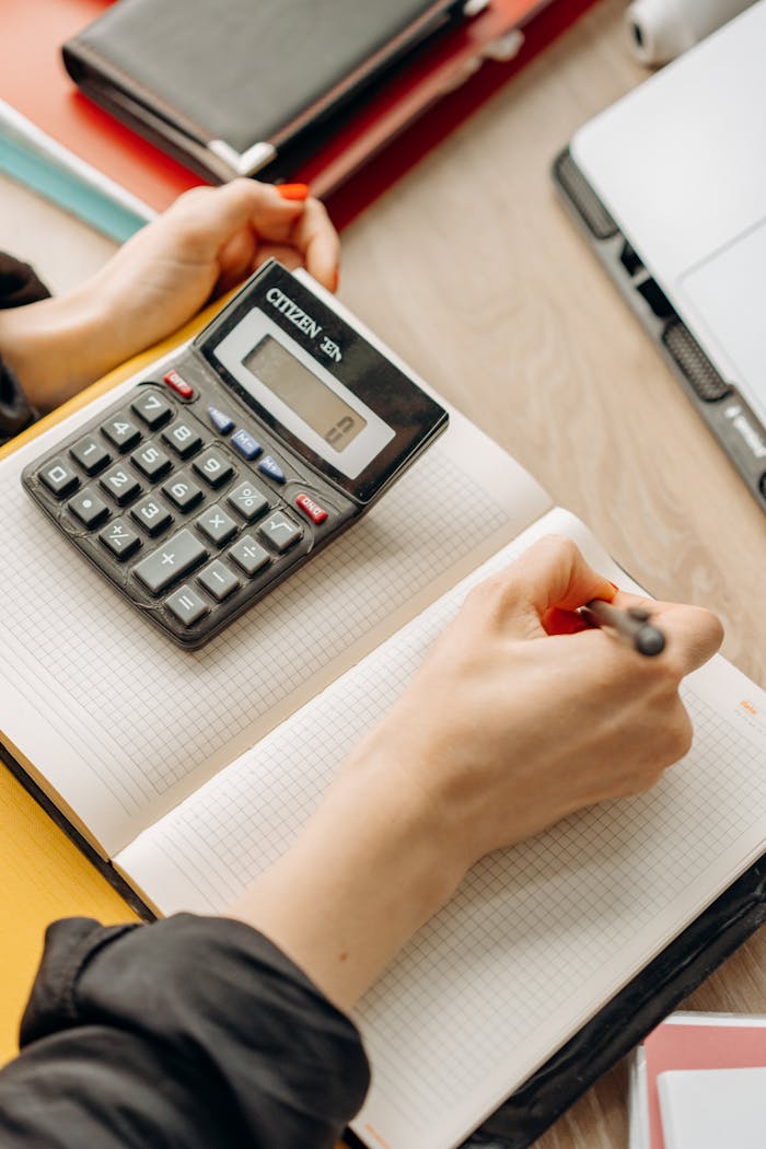creative-02 Person writing in notebook with calculator nearby on a desk. Ideal for business or finance themes.