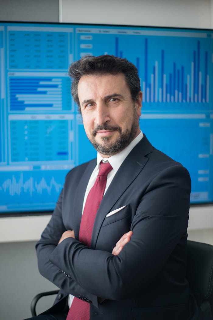 our-story Confident businessman in suit posing in front of data screens in a modern office.